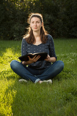 Teen girl reading the Bible sitting outdoors