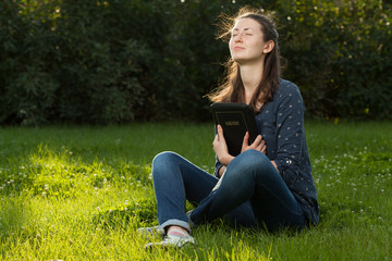 Teen girl gugging the Bible sitting outdoors with copy space