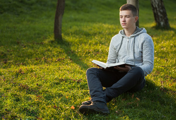 Naklejka na ściany i meble Young man reading Bible in a park