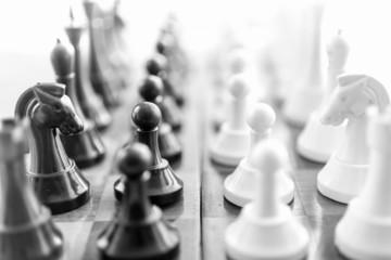 Black and white shot of chess pieces standing in rows face to fa