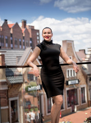 woman in black dress posing against old rooftops at sunny day