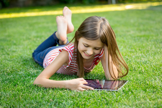 girl lying on grass and using tablet