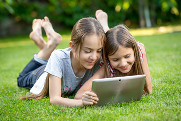 cute girls relaxing on grass at park and using digital tablet