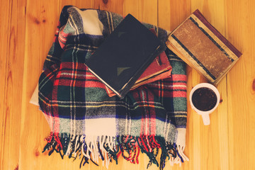 Woolen plaid, cup of tea, old books on wooden background. Top view. Toned