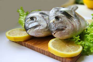 Fresh dorado on chopping board with lemon and vegetables
