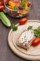 Fried pork steak with vegetables and parsley on a wooden board