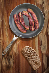 Fried Bacon Rashers in Teflon Frying Pan with Bread Slice on old obsolete Wooden Table