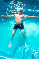 Man in sunglasses is laying on blue water surface in swimming pool.