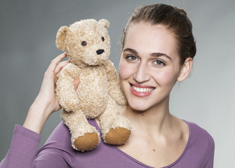 smiling proud young blonde woman playing with her teddy bear on her shoulder with tenderness for child memories