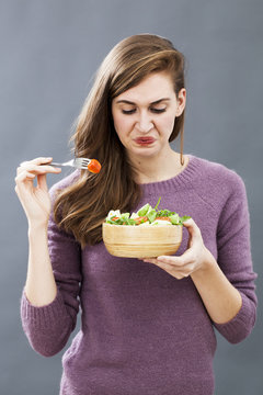 Displeased Young Girl Being Picky At Eating Mixed Green Salad With Cherry Tomatoes As Vegetarian Diet