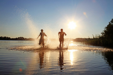 Glückliche junge Menschen laufen und springen am See beim Sonnenuntergang © Thaut Images