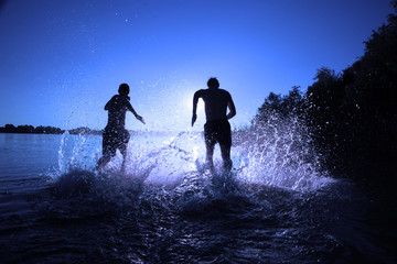 Glückliche junge Menschen laufen und springen am See beim Sonnenuntergang