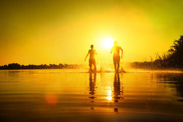 Glückliche junge Menschen laufen und springen am See beim Sonnenuntergang