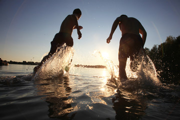 Glückliche junge Menschen laufen und springen am See beim Sonnenuntergang