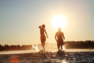 Glückliche junge Menschen laufen und springen am See beim Sonnenuntergang