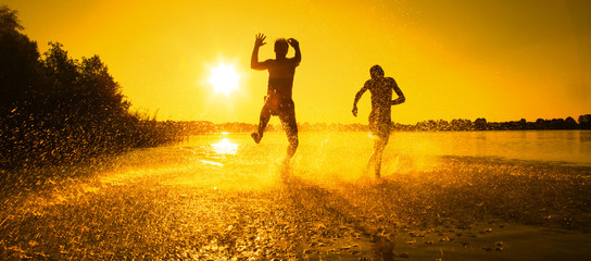 Glückliche junge Menschen laufen und springen am See beim Sonnenuntergang