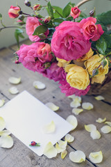 bouquet of pink and yellow roses in a wicker basket and white sheet of paper for a message