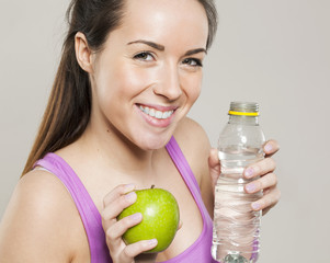 thrilled young gym girl with holding bottle of water and green apple after exercising