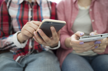 Two women are using a smart phone sitting on the sofa