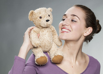 friendly young blonde woman holding her teddy bear on her shoulder with tenderness for beautiful memories together