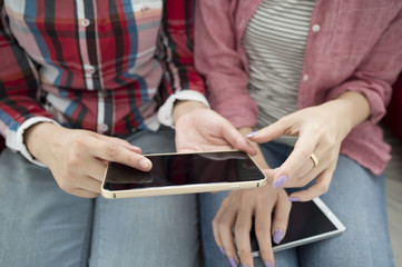Two women are using a smart phone sitting on the sofa