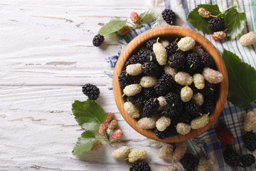 White and black mulberries in a wooden bowl horizontal top view
