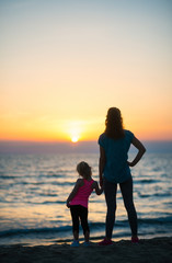 Fototapeta premium Mother holding daughter's hand at sunset looking out to sea