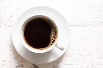 Coffee in cup from above, on rustic white wood.