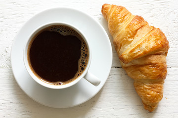 Croissant and coffee on rustic white wood, from above.