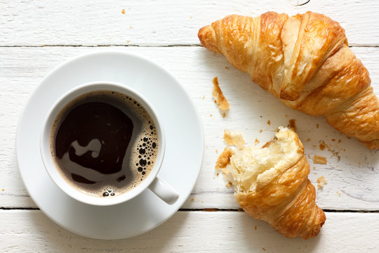 Croissants and coffee in cup on rustic white wood, from above.