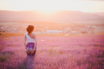 Young woman with beautiful hair wearing white and blue dress standing in a lavender field at the...