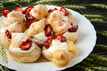 Homemade eclairs with strawberries on dark wooden background