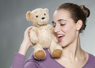 playful young blonde woman holding her teddy bear on her shoulder with tenderness for beautiful memories together