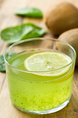 kiwi spinach green smoothie with lemon in glass on brown wooden background