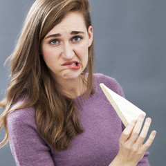 displeased young girl biting lips in holding dairy product as unappetizing milk diet