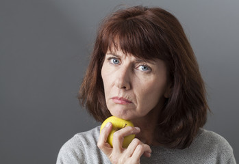 resigned mature woman thinking with yellow golden apple under her chin for vitamins diet