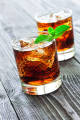 Two glasses of cola with ice and fresh mint on wooden table.