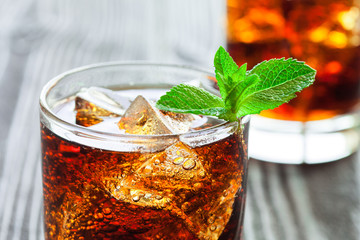 Two glasses of cola with ice and fresh mint on wooden table. - obrazy, fototapety, plakaty