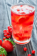 Glass of drink with strawberry and red currant berries on wooden