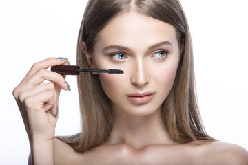 Fototapeta premium Beautiful young girl with a light natural make-up and beauty tools in hand. Picture taken in the studio on a white background.
