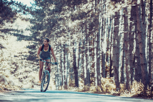 Gracefully biking through the forest, a skilled female athlete enjoys the mountain bike ride.