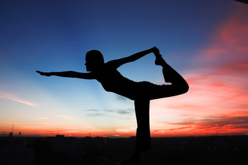 Silhouette young woman practicing yoga on the mountain at orange sunrise