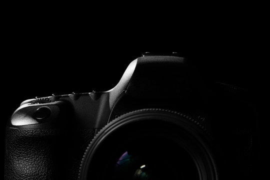 Image of a professional modern DSLR camera low key image - Modern DSLR camera with a very wide aperture lens on in a dark space. Top part of a camera is visible and the rest goes into the shadow