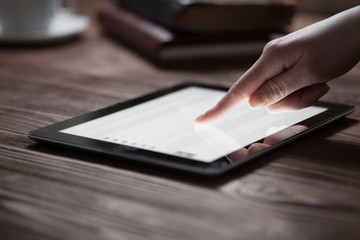 woman hand presses on screen digital tablet over wooden table