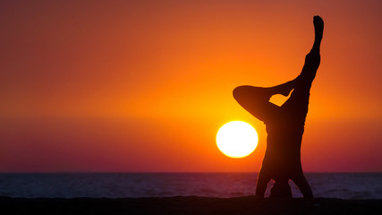Yoga on the beach. A silhouette of the man practicing yoga outdoors (at the seashore) at the sunset. 