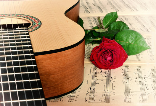 Guitar with classical sheet music and red rose