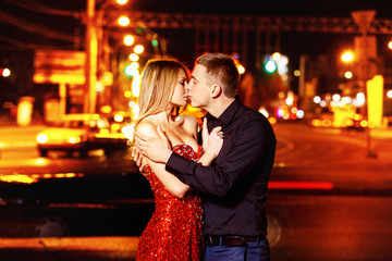 Beautiful young woman in red sparkling dress kisses boyfriend