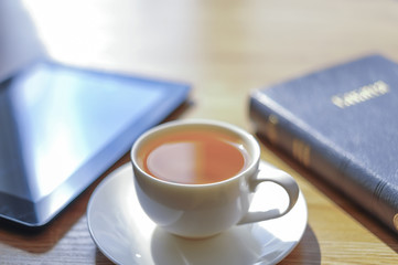Near a cup the tablet and the Bible lies.
