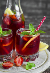 strawberry lemonade with fresh mint and lemon in glass beakers on a dark wooden background