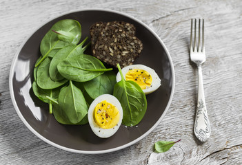 healthy snack - fresh spinach and an egg on a brown plate on a light wooden background